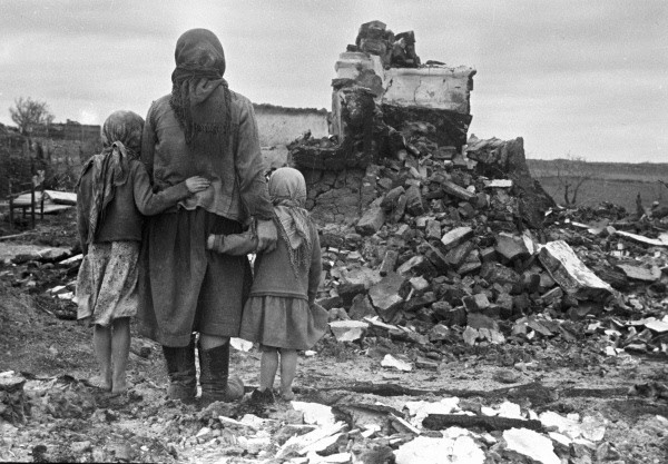 Женщина с двумя девочками смотрит на развалины дома